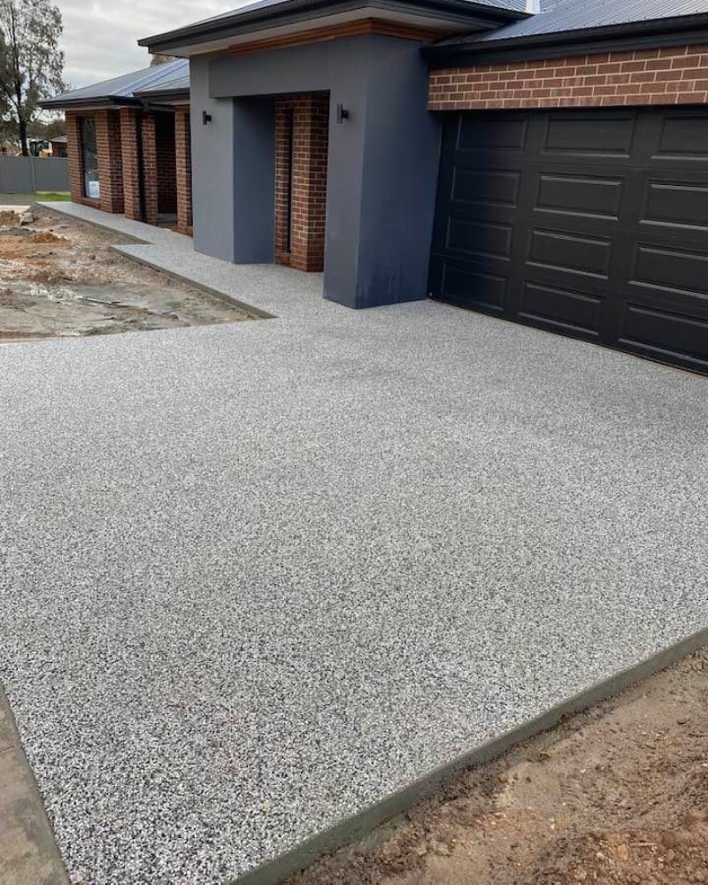 Salt-and-pepper exposed aggregate driveway sweep against a modern rendered Epsom home.