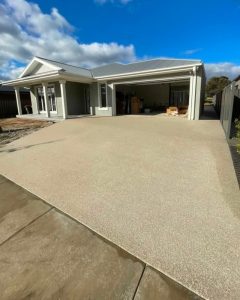 Light-toned exposed aggregate concreting curving toward a weatherboard and rendered-style home, White Hills.