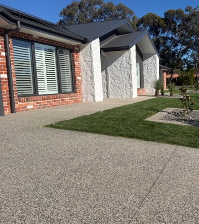 Exposed aggregate driveway, footpath and garden edging surrounding a stone-clad home, Strathdale.